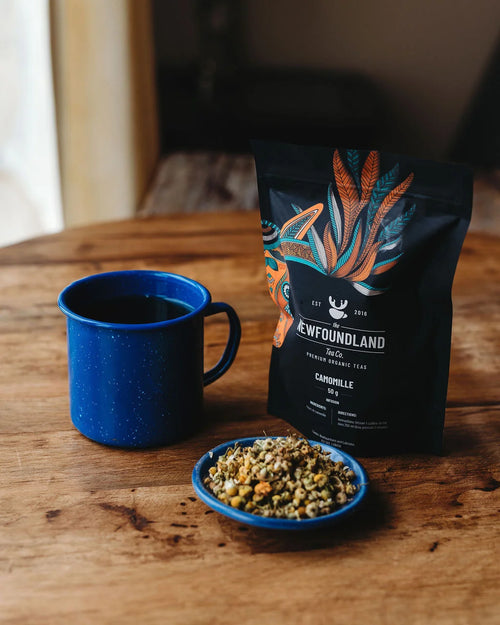 Chamomile tea pouch beside a blue enamel mug and a dish of whole dried chamomile flowers