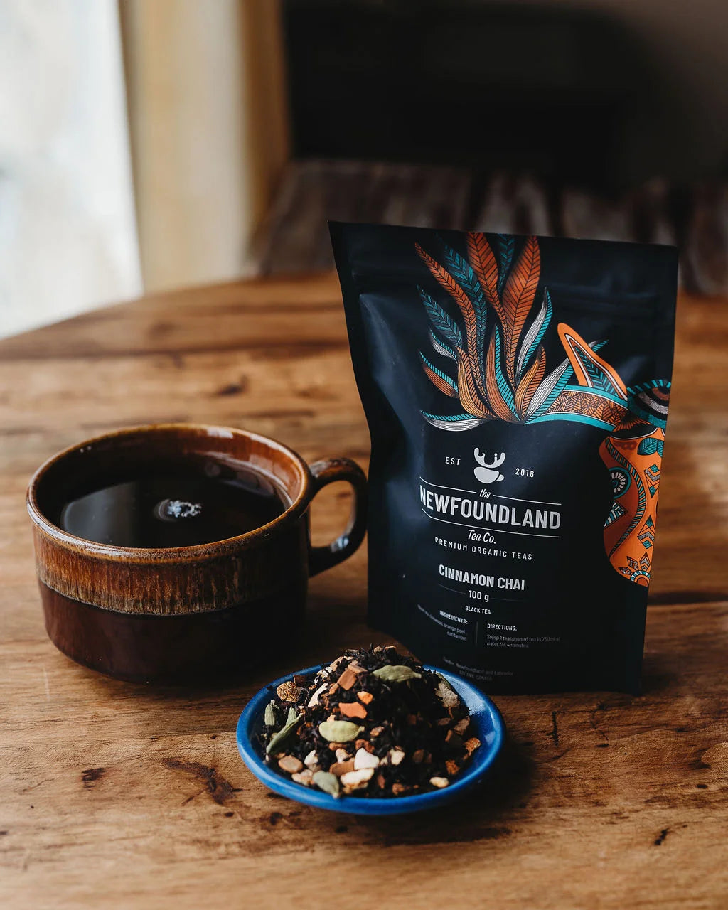 Cinnamon Chai black tea pouch beside a brown mug and a dish of spiced loose leaf chai