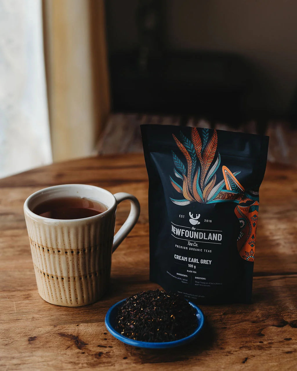 Cream Earl Grey loose leaf black tea pouch beside a cream ceramic mug of tea