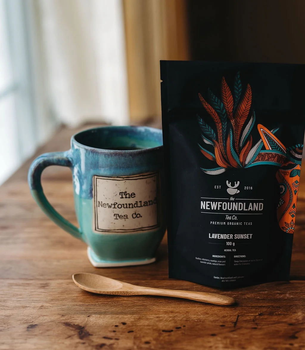 Lavender Sunset rooibos tea pouch with a teal Newfoundland Tea Co. mug and a wooden spoon
