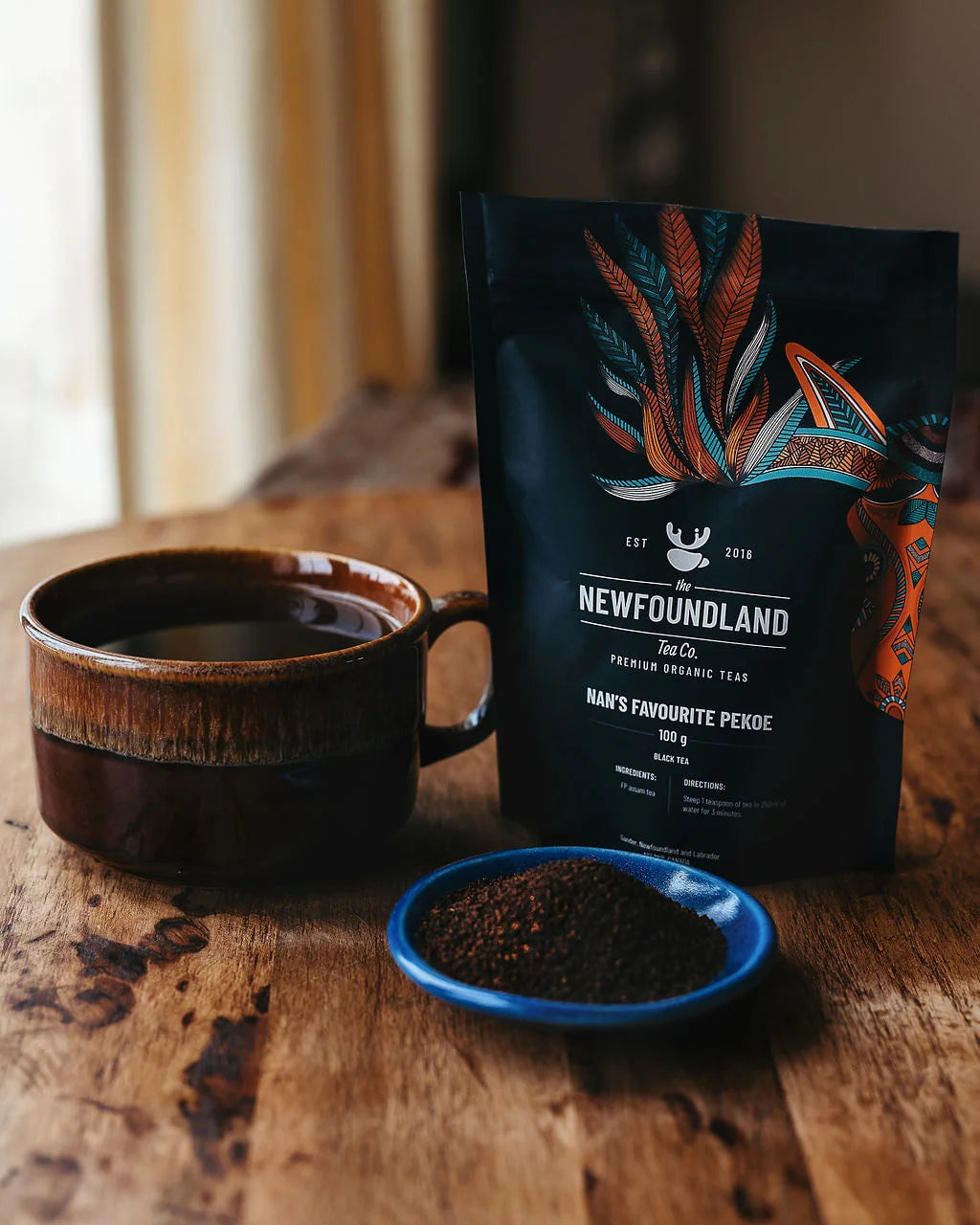 Nan’s Favourite Pekoe orange pekoe tea pouch beside a brown mug and a dish of loose black tea