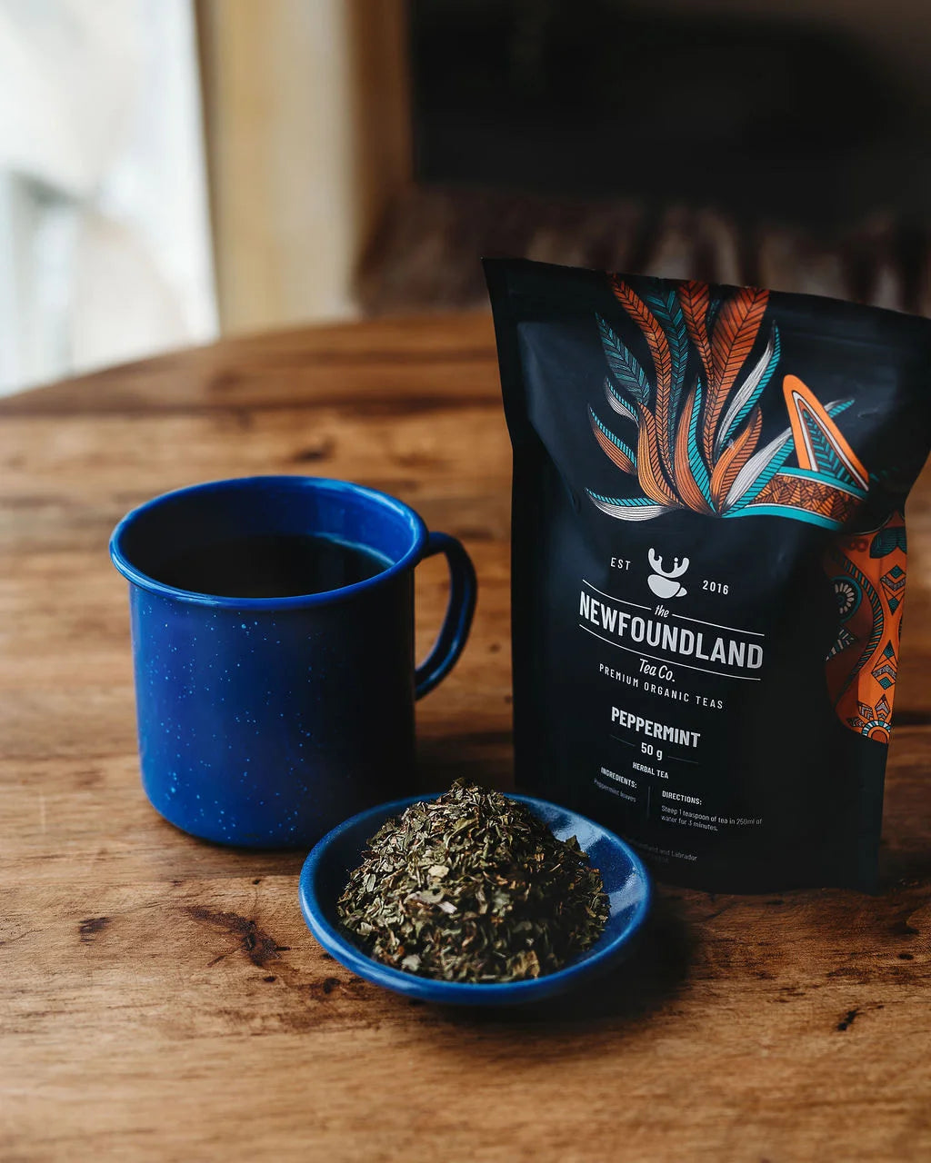 Peppermint tea pouch with a blue enamel mug and a dish of dried peppermint leaves